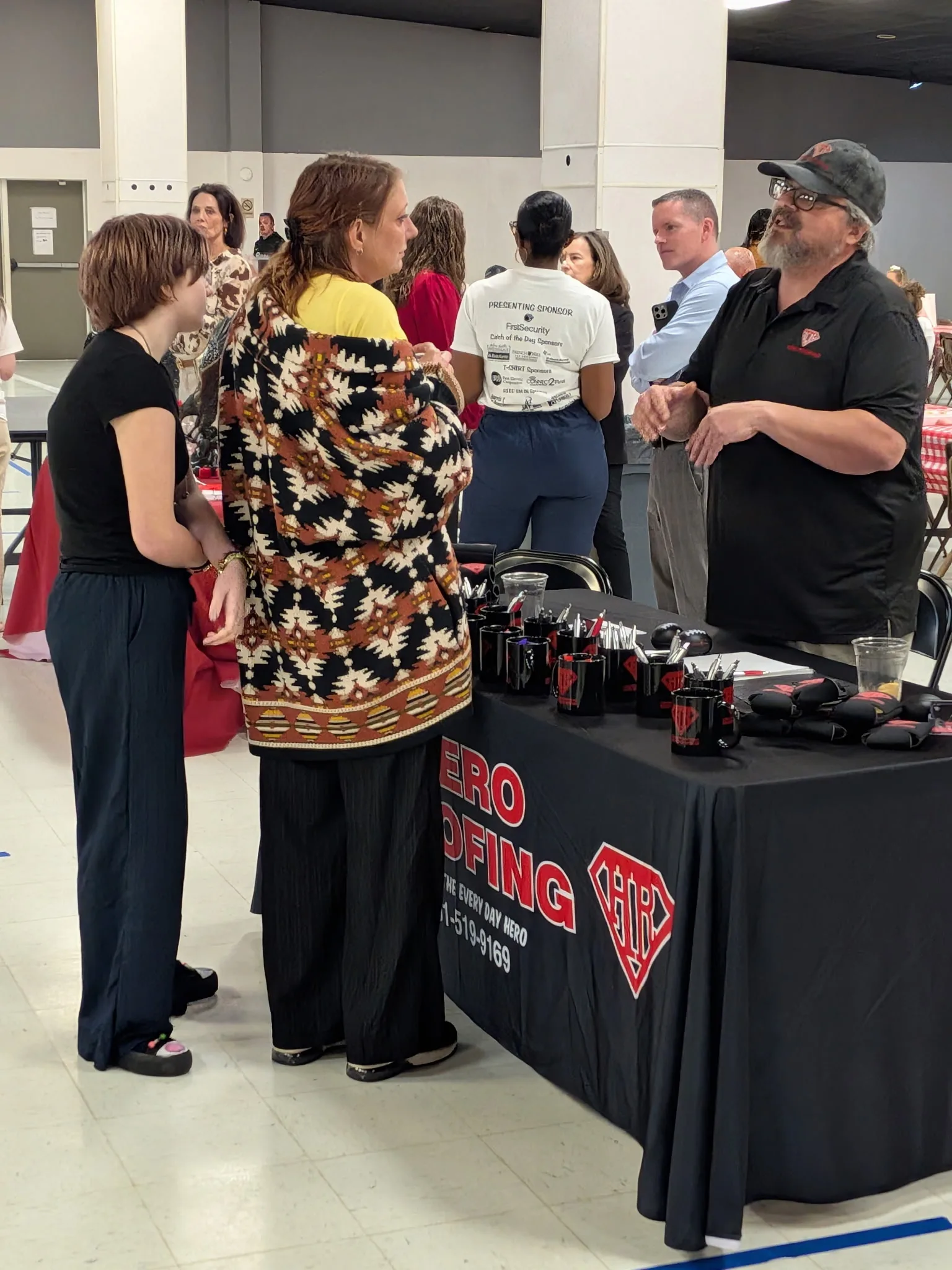 Hero Roofing team member talking with visitors beside the company table at the Sherwood Fish Fry